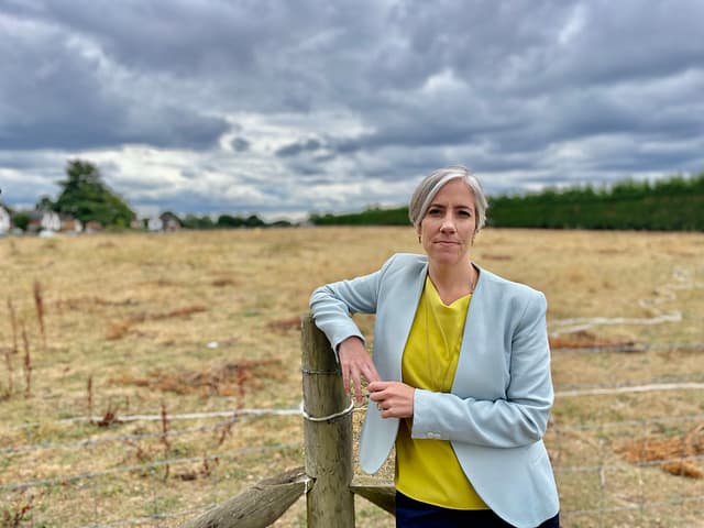 Daisy Cooper MP is standing in front of a green space, leaning against a fence and looking directly at the camera.