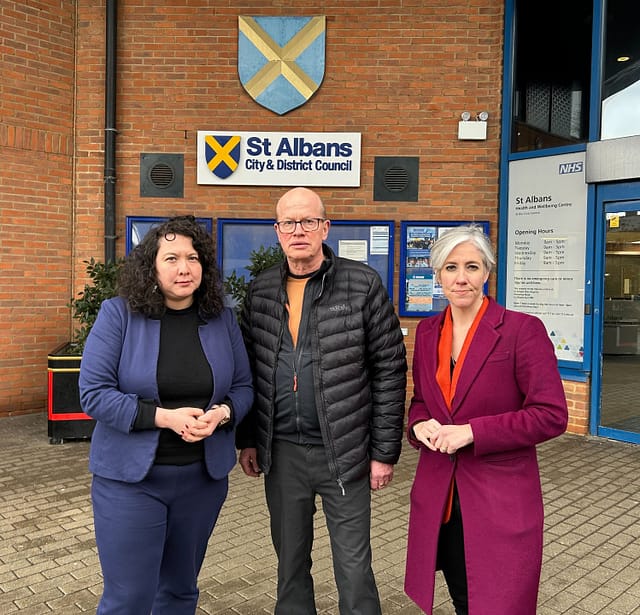 Victoria Collins MP, Councillor Paul de Kort and Daisy Cooper MP (from left to right) are standing in front of the St Albans District Council building. They are all looking directly at the camera, with serious expressions.